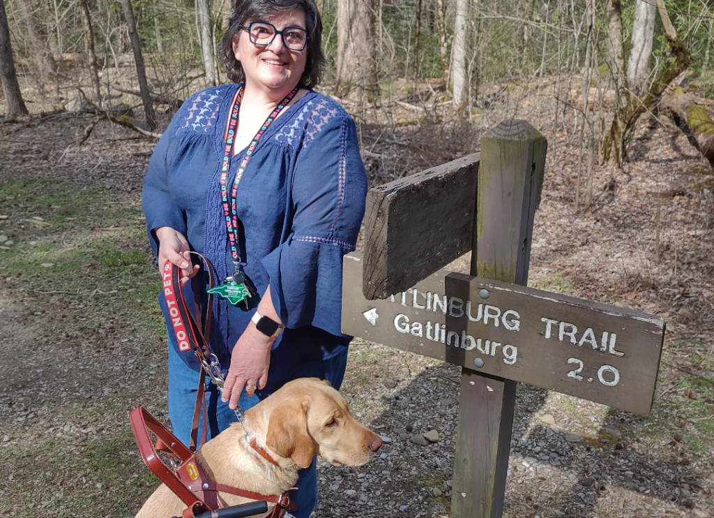 Woman and service dog in front of a trail sign in Gatlinburg, TN in early spring