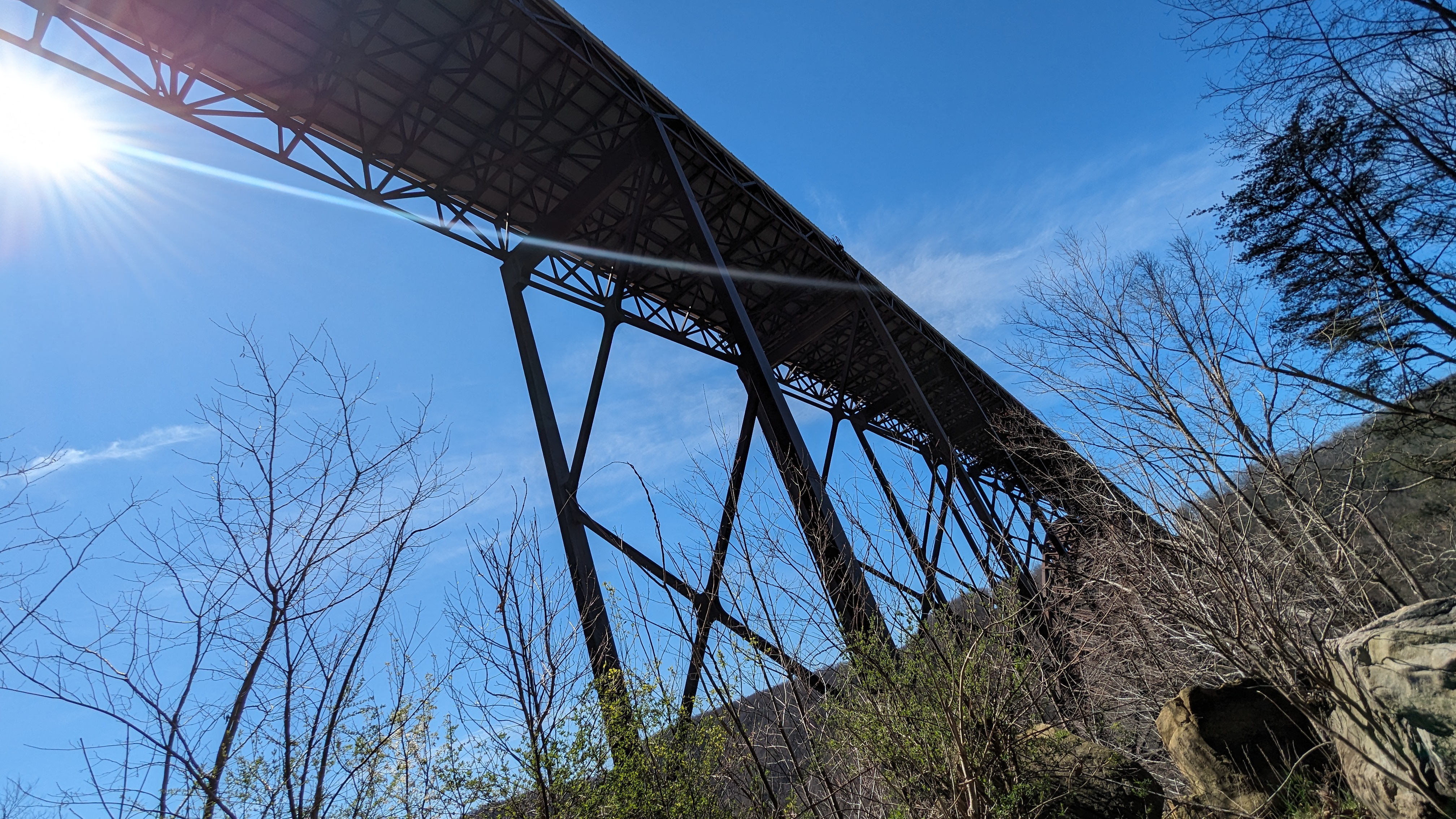 View of a bridge looking up from the bottom. Trees and blue sky