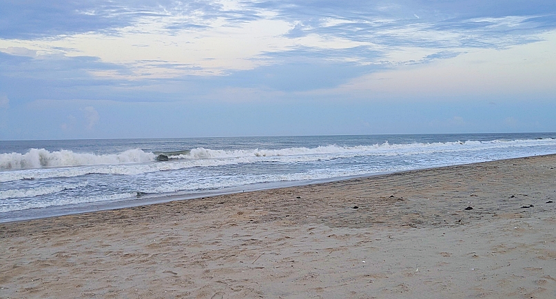 Beach with waves, blue sky with clouds and tan sand. Near twilight