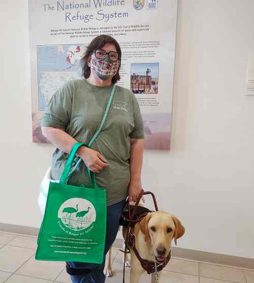Woman and her yellow lab service dog inside the visitor center at Bosque Del Apache Wildlife Refuge. She is wearing a mask and holds a green and white bag.