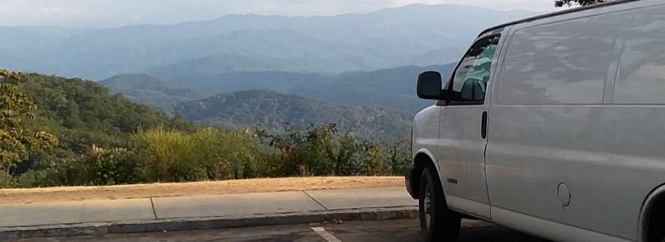 White cargo van parked at a mountain overlook, with layers of blue ridges stretching into the distance.